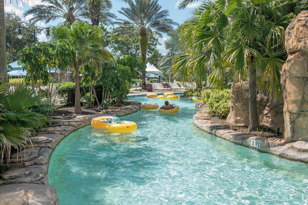 lazy river, pool water, yellow inner tubes with blue handles, palm trees, rocks, boy on tube