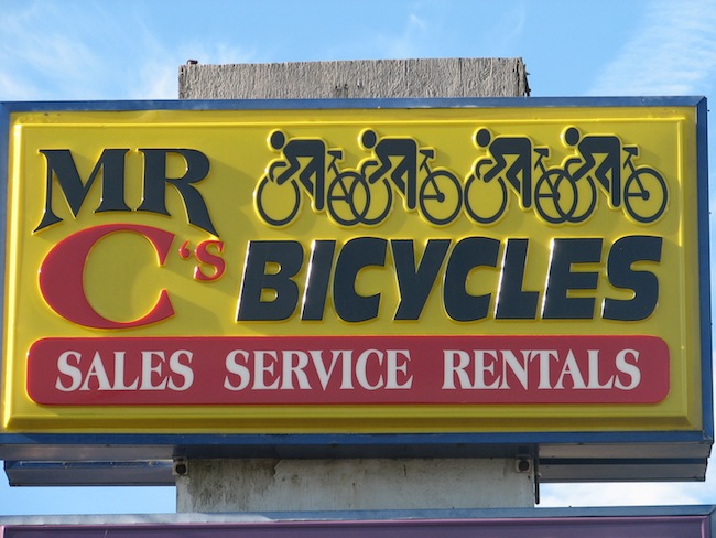 Sign saying Mr C's Bicycles Sales, Service Rentals, and 4 people on bikes on sign
